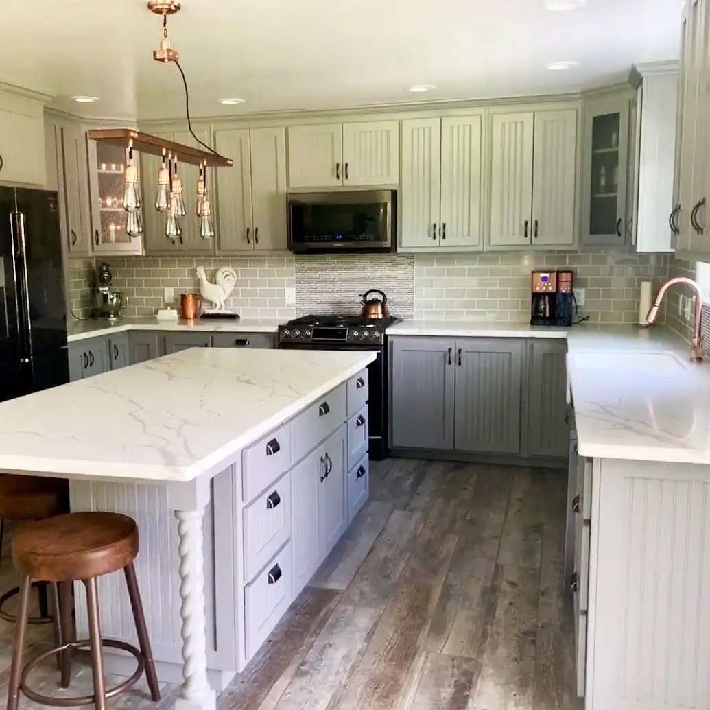 Kitchen remodeling in Chico: grey beadboard cabinets, a white marble-look island with a turned post, subway tile backsplash and wood-look plank floor